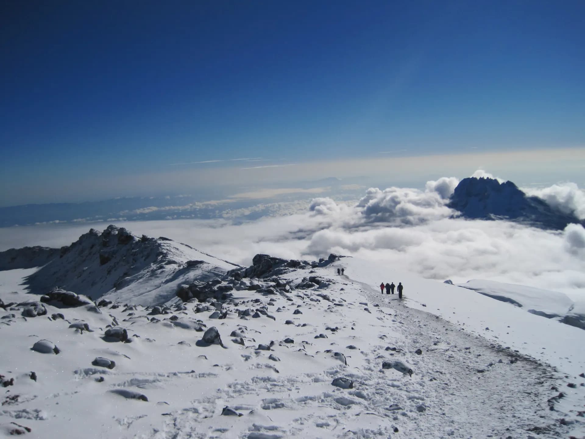 Climbers on Kilimanjaro's snowy summit ridge, with Mawenzi peak visible behind them